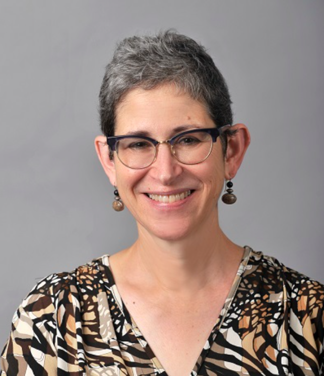 Headshot of a School of Social Work faculty member with short dark hair and glasses, smiling, wearing a patterned blouse against a neutral background.